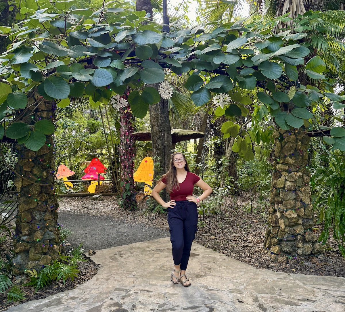 Amy Zelt smiling in a lush botanical garden, surrounded by vibrant greenery and sunlight, reconnecting with beauty, creativity, and joy.